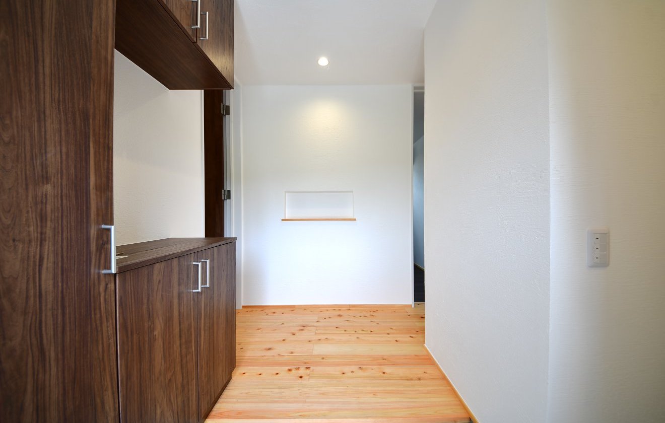 住まいの中心に配置された“真ん中玄関”は、どの部屋へもアクセスしやすい便利なレイアウト。右手には洋室が2部屋、左手には家族が集うLDK、正面には主寝室が続き、帰宅後の動きがスムーズになるよう計算された間取りです。玄関にはシューズインクローク（SIC）を備え、靴やアウトドア用品をすっきり収納。漆喰壁の柔らかな質感と、桧の無垢床の心地よい香りが出迎えてくれる、“暮らしの真ん中”にふさわしい、上質で温もりある玄関空間です。