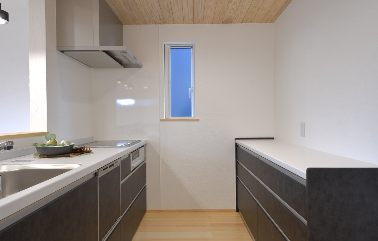天井には美しい木目が広がる“杉”を採用し、やわらかなあたたかさを感じるキッチン空間。落ち着きのあるシックな色合いのキッチンと組み合わせることで、上質で洗練された雰囲気に仕上げています。腰壁越しにリビング・ダイニングを見渡せるため、家族の気配を感じながら料理ができ、自然と会話も弾むキッチン。デザイン性と使いやすさを兼ね備えた、心地よい空間です。